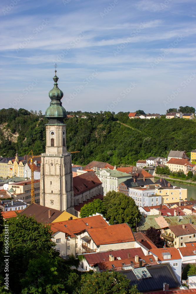 Fototapeta premium Church tower with green dome roof and clock in Burghausen, Bavaria, Germany, overlooking the river and colorful old town houses, photographed in 2024.
