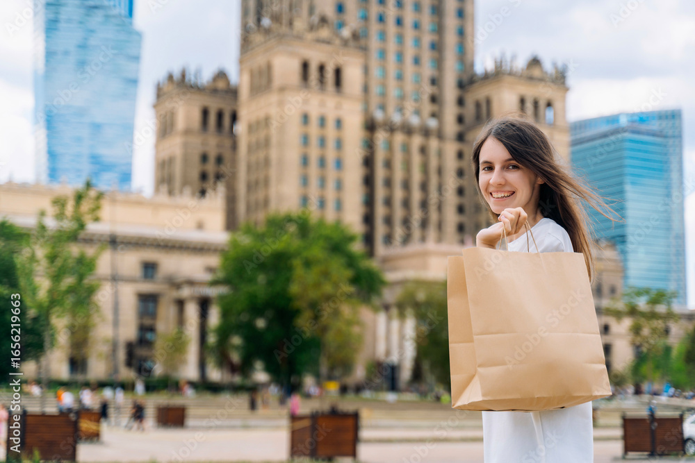 Fototapeta premium Smiling young woman with eco-friendly paper shopping bag in the city