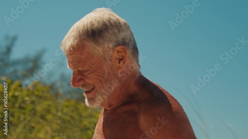 Elderly Brazilian happy surfer walks with surfing board after surfing in the ocean in Brazil and looks into the camera