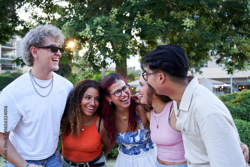 Obraz premium Happy photo of a multicultural group of friends looking at each other laughing while embracing in circle outdoors, People gathered having fun. Copy space image.