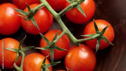 Fresh sprigs of red cherry tomatoes with green leaves in a wooden bowl. Rotation