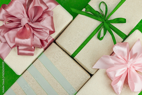 Eco-friendly gift boxes wrapped in kraft paper and decorated with satin ribbons on green background