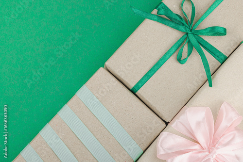 Eco-friendly gift boxes wrapped in kraft paper and decorated with satin ribbons on green background