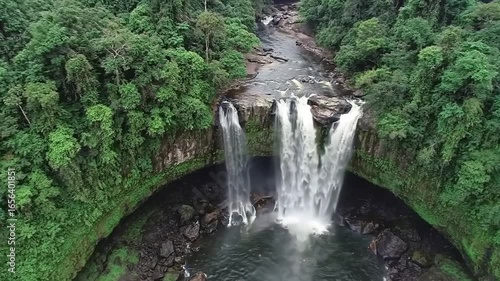 Aerial view of a powerful waterfall cascading into a dark pool surrounded by trees