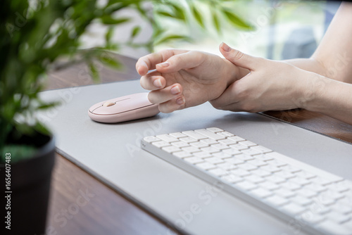 Person clutching painful wrist from extended computer mouse use, indicating a repetitive strain injury and ergonomic health concerns in modern digital workspace