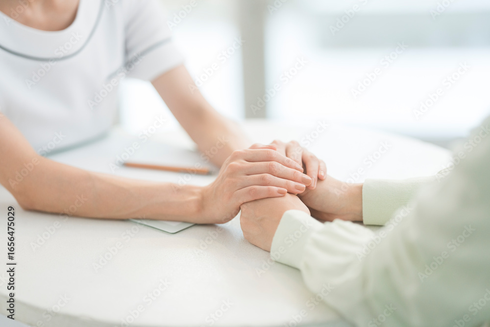 Obraz premium エステティシャン/セラピスト。彼女はカウンセリング相手の手に両手を重ねて親身になり話を聞いている。