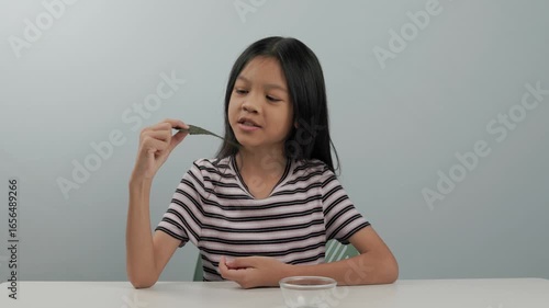 child girl cute face wearing a striped shirt picked up a seaweed chips in a small bowl placed on a white table and ate them with delight. She was very happy to have her favourite snack during the day.