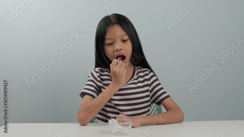 cute primary kid girl wearing striped shirt is sitting and picking up a white dental floss picks to clean after meals and after brushing her teeth, to keep her teeth clean and strong at all times.