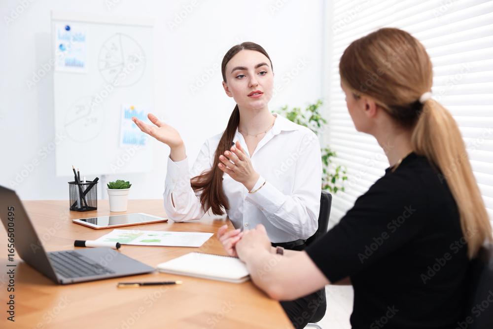 Business coach working with woman at wooden table in office Business coach working with woman at wooden table in office