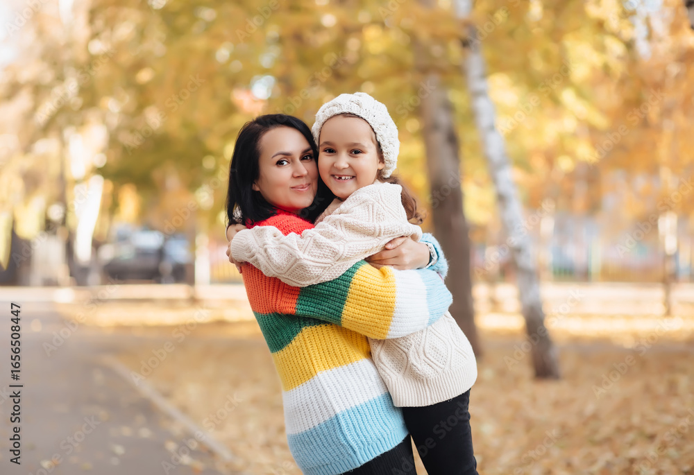 Naklejka premium Cute little girl and mom hugging in the autumn park. Family have fun outdoor.