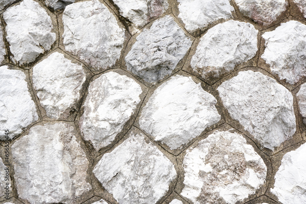 Obraz premium 自然石を組み合わせて作られた石垣のクローズアップ。白っぽい石とコンクリート目地が生み出す独特のパターンは、建築素材や背景テクスチャとして活用できるイメージ。