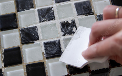 hand spreading grout on black and white small tiles