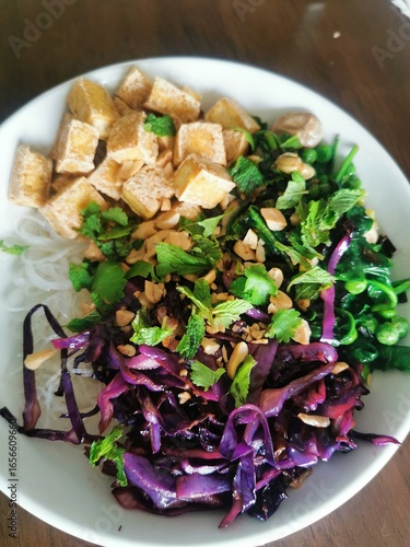 A colorful and healthy vegan noodle bowl with fried tofu, red cabbage, spinach, and fresh mint, topped with chopped peanuts.