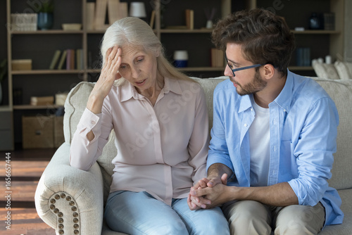 Tender family moment. Attentive compassionate grownup son sit on sofa with sad suffering senior mom hold hand of dear parent listen to mum sharing troubles soothe comfort reassure with warms kindness