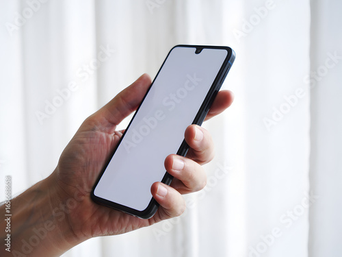 Hand Holding Black Smartphone with White Screen Showing Device Ready Text, Close Up Mobile Phone Mockup Against White Curtain Background.