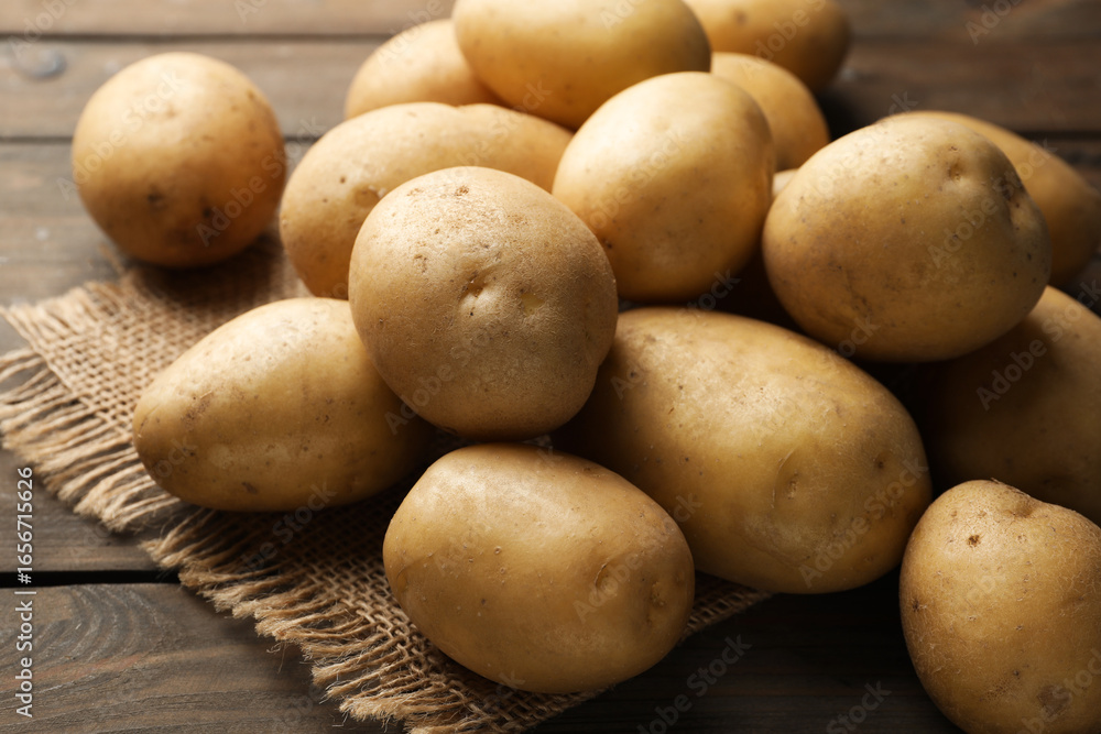 Many raw potatoes and burlap fabric on wooden table, closeup Many raw potatoes and burlap fabric on wooden table, closeup