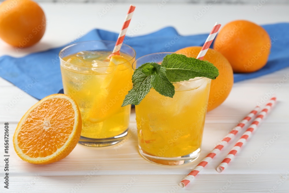 Fototapeta premium Refreshing soda water with orange slices in glasses, mint and fresh fruits on white wooden table, closeup