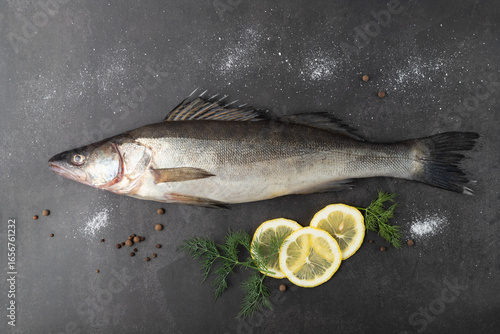 Fotografija Whole unpeeled fresh zander or pike perch fish with lemon slices, dill and spices on grunge stone table background
