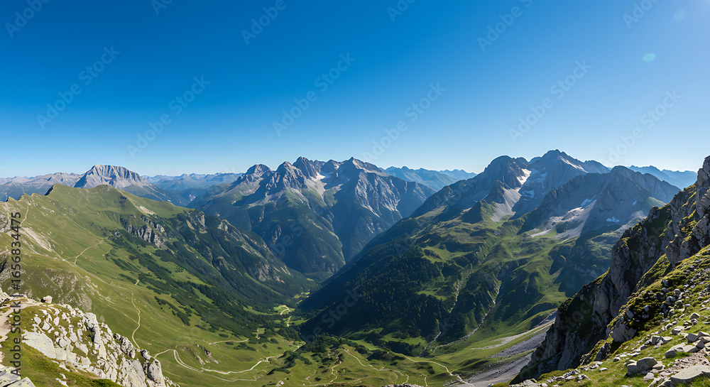 Fototapeta premium Panoramic alpine valley view, lush green valleys, and snow-capped mountain peaks under a clear blue sky.
