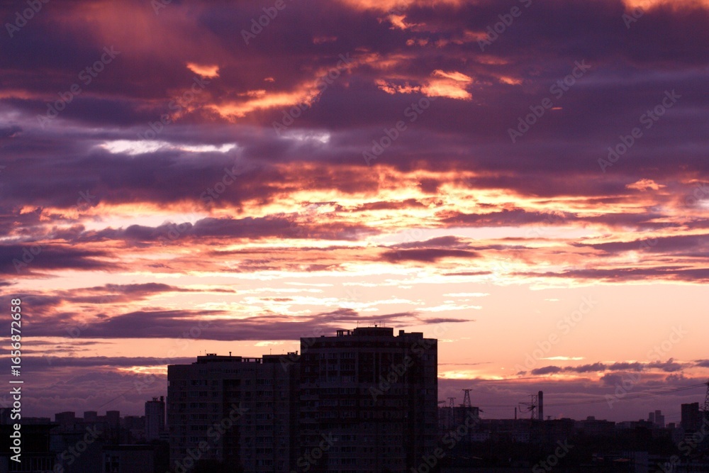 Fototapeta premium Dramatic sunrise illuminates the city skyline with colorful, textured clouds above silhouette buildings. Concept of: Urban dawn.