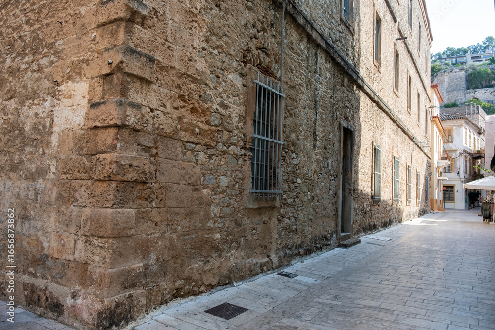 Fototapeta premium Historic building on a narrow paved street in Nafplio Greece with stone walls and barred windows