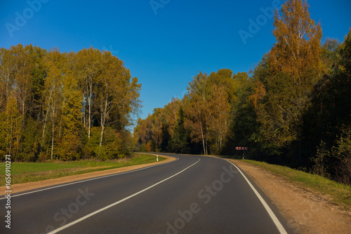 Autumn landscape and sunny evening, orange road and highway, asphalt and roadside.