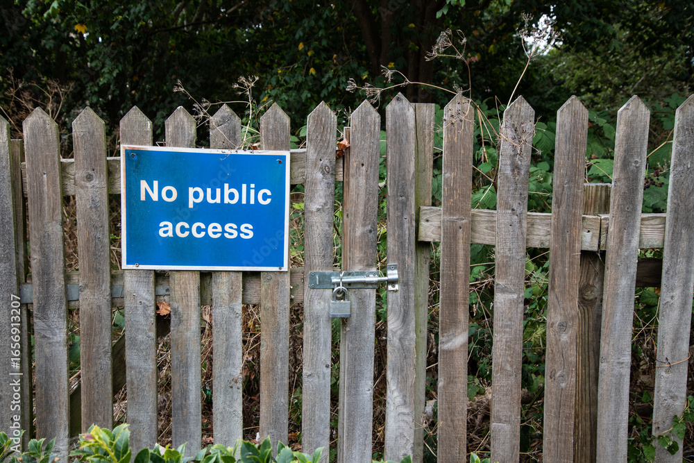 Fototapeta premium No Public Access sign on a locked wooden gate and fence, with trees and bushes behind. Restricted entry, private property concept in rural setting.