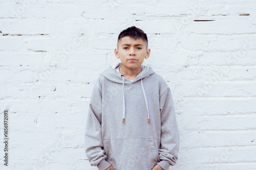 Latin boy standing with hands in pockets against white wall