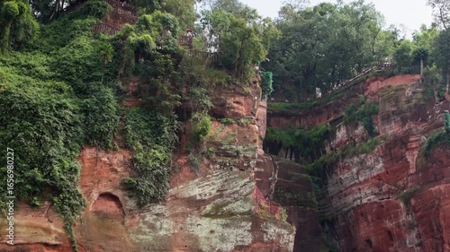 Wide slow motion shot of the entire Leshan Buddha from side angle, showing scale and surrounding natural context