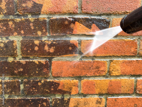 Close up view of a pressure washer being used to clean dirty bricks on a garden wall