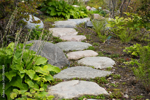 A tranquil garden path made of natural, irregular stepping stones surrounded by lush plants 
