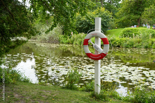 Canvas Print Two red and white lifebuoys on posts stand ready for safety by a calm pond with water lilies in Copenhagen, Denmark
