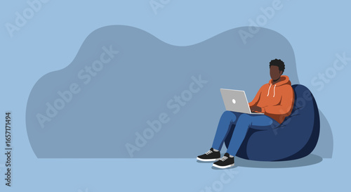 Young man comfortably working or studying on his laptop from a bean bag chair, representing remote work and a relaxed digital lifestyle.