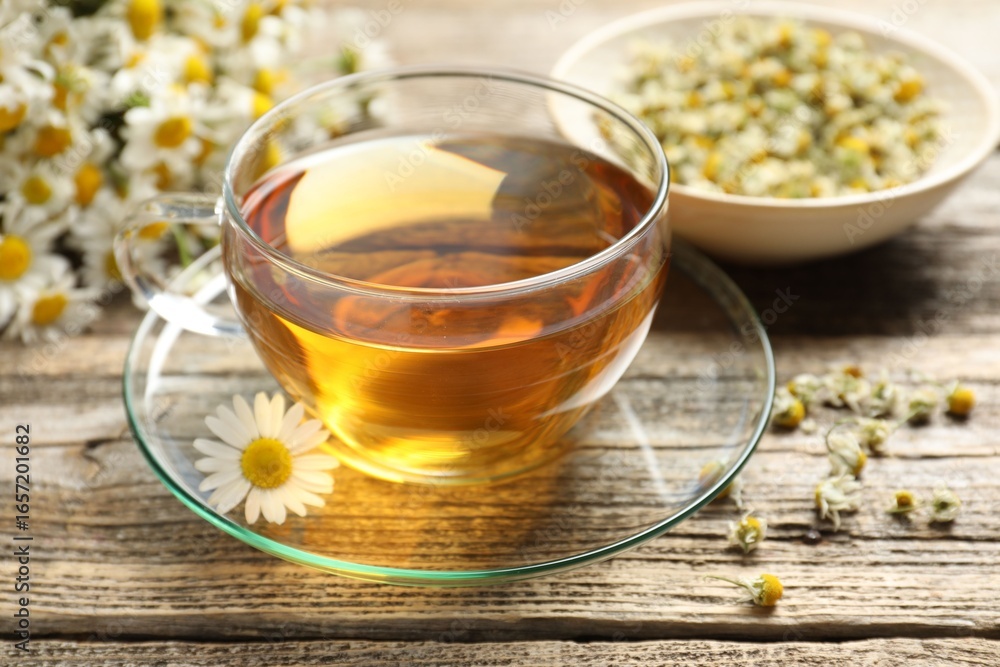 Aromatic tea in glass cup and chamomile flowers on wooden table, closeup Aromatic tea in glass cup and chamomile flowers on wooden table, closeup
