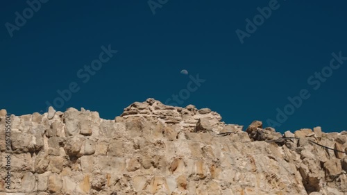 Moon rising above ancient stone fortress wall in Tangier, Morocco under dark sky