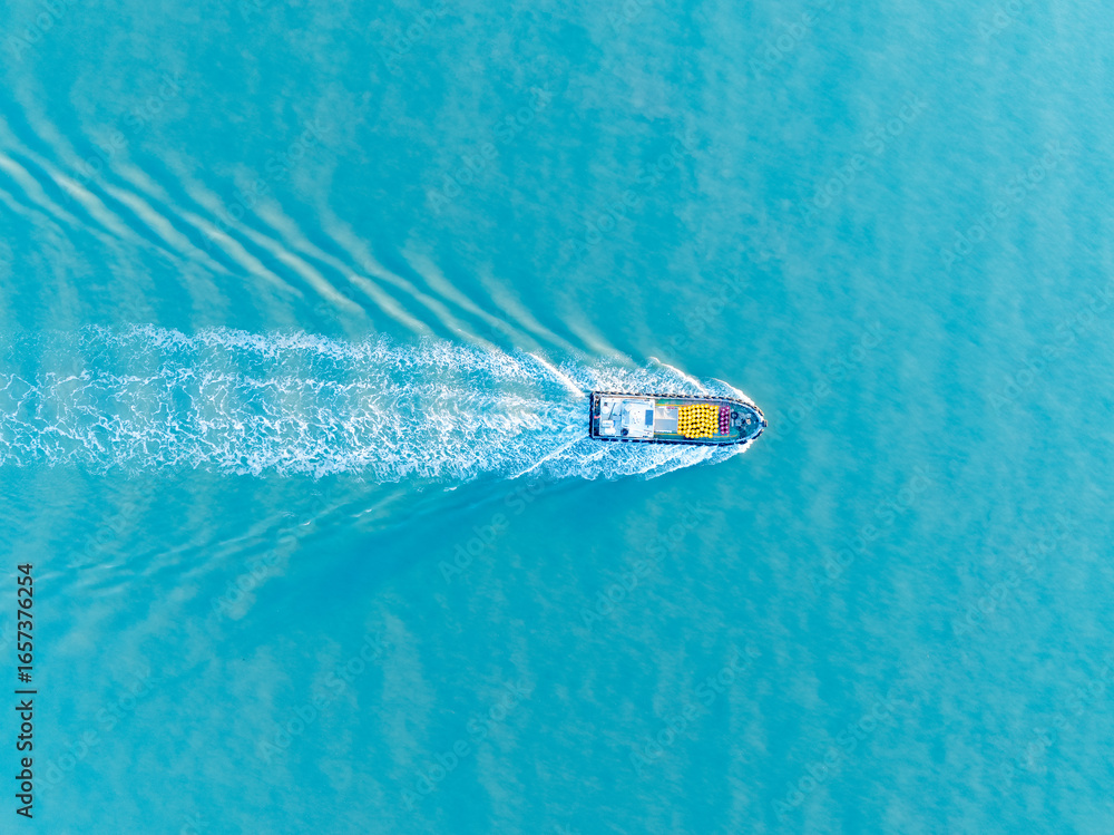 Naklejka premium A lone boat moves across the wide blue ocean creating a foamy white wake as it sails calmly on the vast water.