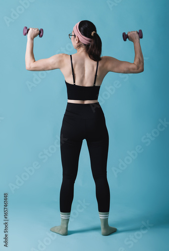 Woman from the back, lifting dumbbells, symbolizing fitness and a commitment to a healthy lifestyle for overall wellness, a healthy and fit lifestyle. Good habits for a balanced life
