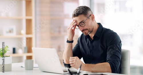 Business, man and laptop with headache in office for finance mistake, auditing deadline and stress. Financial manager, mature person and tech with tension migraine for corporate bankruptcy and debt