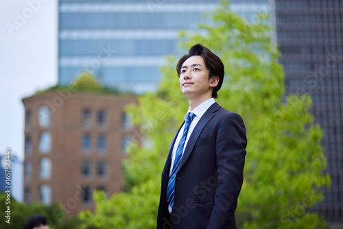 ビルを背景に遠くを見つめるスーツを着た日本人ビジネスマンの男性