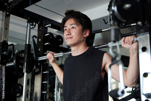 フィットネスジムで筋力トレーニングを行うスポーツウェアを着た若い日本人男性