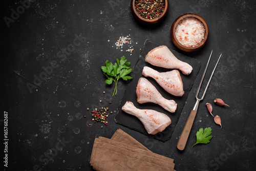 Raw chicken drumsticks with spices on black stone background, top view, flat lay