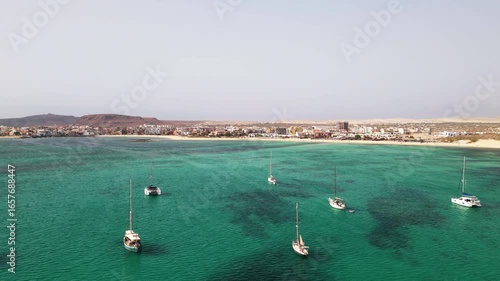 Aerial view of the city of Sal Rei, many luxury yachts moored in turquoise ocean,background the port, its old color city and the desert with the mountains