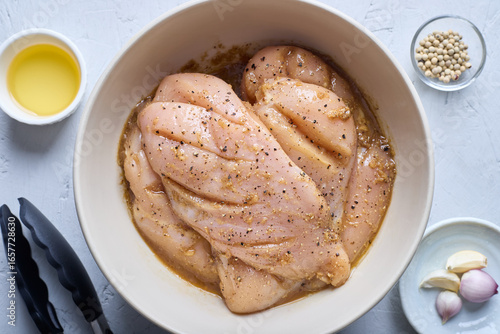 Fotografija Close -up of marinate chicken breast until tender with the ingredients and food tongs on white background