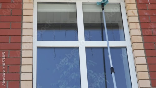 Man washing tall house window with cleaning tool