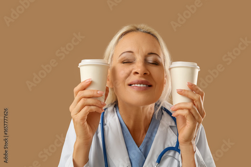 Mature female doctor with cups of coffee on brown background