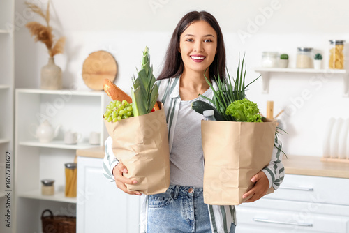 Young Asian woman with shopping bags full of fresh food in kitchen