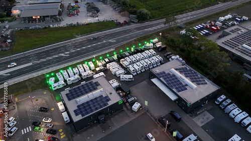 Modern Camper dealership with vans and motor homes in industrial area of town. Dusk scene. Aerial top down shot. Company with construction vehicles parking on area. Suburb of American town.