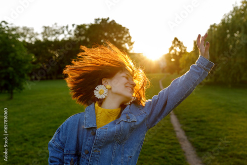 Carefree woman with hand raised enjoying in park at sunset