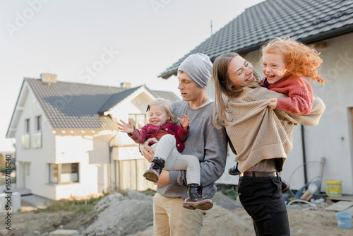 Mother and father carrying daughters outside house