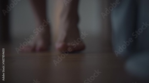 A man slowly walks barefoot on wooden planks in a softly lit room. The soft light envelops the feet, creating a feeling of quiet evening coziness. This scene gives a feeling of peace and inner harmony